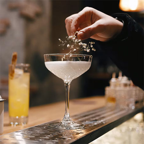 MAISON PERRIER<sup>®</sup> cocktail garnished with delicate white flowers at a bar